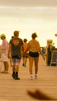 a group of people walking across a wooden pier next to a skateboarder on the ground