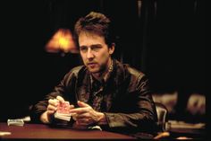 a man sitting at a table with cards in his hands and looking off to the side