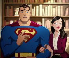 a woman standing next to a man wearing a superman suit in front of bookshelves