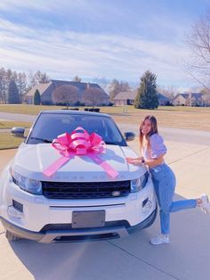 a woman leaning on the hood of a car with a pink ribbon tied around it