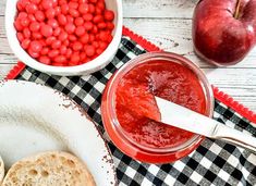 two bowls filled with jelly next to an apple and crackers on a checkered table cloth