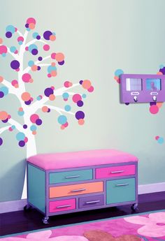 a child's room with a tree painted on the wall and colorful dressers