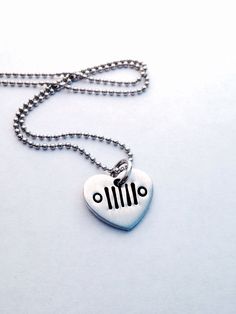 a silver heart shaped pendant on a ball chain with a black and white car symbol