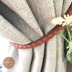 a close up of a curtain with a flower on it's side and a plant in the background