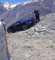 a man standing next to a black car on top of a mountain