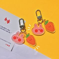 two keychains with carrots and bunny faces attached to each other on a yellow background