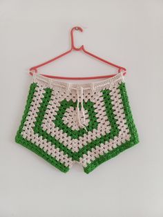 a green and white crocheted shorts hanging on a hanger with a red hook