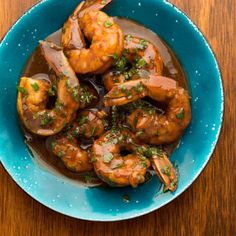 a blue bowl filled with cooked shrimp on top of a wooden table