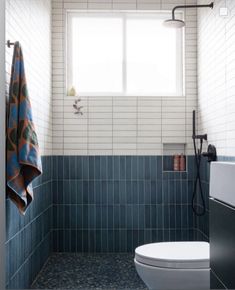 a white toilet sitting next to a window in a bathroom under a blue tiled wall