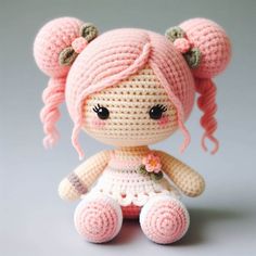 a crocheted doll with pink hair sitting on a table next to a gray background