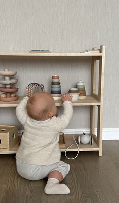 a baby sitting on the floor in front of a shelf