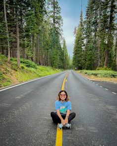 a woman kneeling down on the side of a road with trees in the back ground