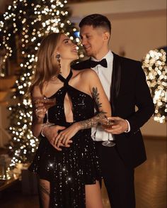 a man and woman standing next to each other in front of a christmas tree