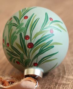 an ornament with green leaves and red berries on it sitting on a table