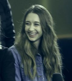 a woman with long hair smiling and holding a microphone in front of two other women