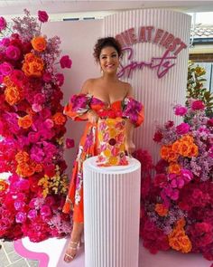 a woman in an orange dress standing next to a white pedestal with flowers on it