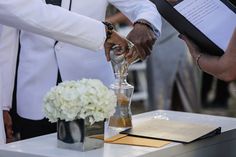 two people pouring sand into a vase on top of a table with flowers in it