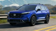 the front end of a blue honda suv driving on a road with mountains in the background