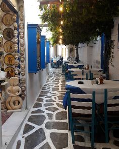 an alley way with tables and chairs lined up along the side walk, in front of blue doors