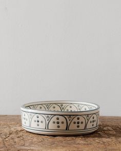 a white and black bowl sitting on top of a wooden table next to a wall