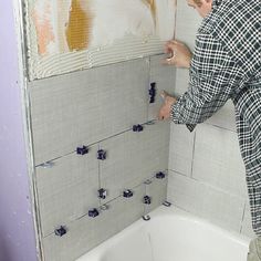 a man in plaid shirt fixing tile on wall next to bathtub