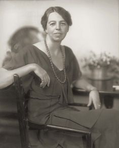 an old photo of a woman sitting in a chair with her hands on her hips