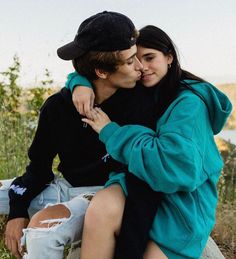 a man and woman sitting on top of a rock next to each other in the grass