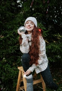 a woman with long red hair sitting on a stool in front of a christmas tree