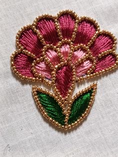 a pink flower with green leaves is on a white fabric background and has gold beading