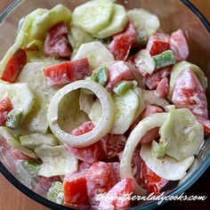 a salad with cucumbers, tomatoes and onions in a glass bowl on a wooden table