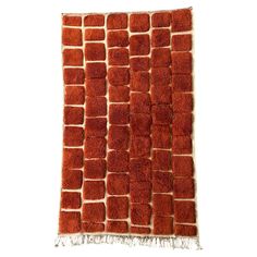 an orange rug with squares and fringes on the bottom, against a white background