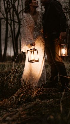 a man and woman standing next to each other in the woods holding lanterns with lights on them