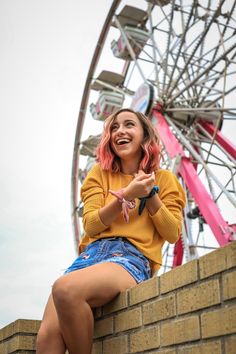 a young woman sitting on top of a brick wall next to a carnival ferris wheel