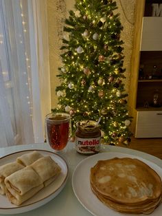 two plates with pancakes on them next to a christmas tree and a glass of nutella