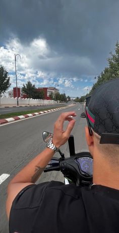 a man riding on the back of a motorcycle down a curvy road under a cloudy sky