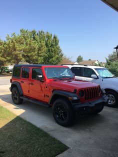 two red jeeps are parked next to each other in a driveway near some trees