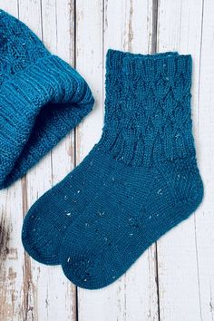 two blue knitted socks laying next to each other on a white wooden surface with one sock in the foreground