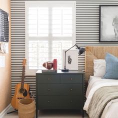 a bed room with a neatly made bed and a guitar on top of the dresser