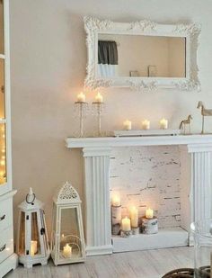 a living room filled with lots of white furniture and candles in front of a fireplace