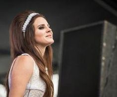 a woman with long brown hair wearing a white dress and headband standing in front of a black box