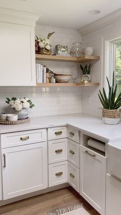 a kitchen with white cabinets and wooden flooring next to a window filled with plants