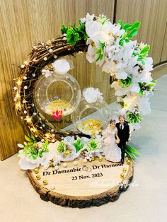 a wedding cake topper is displayed in front of a wooden plaque with flowers and foliage