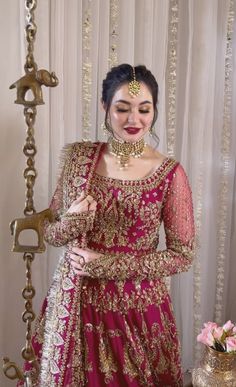 a woman in a red and gold bridal outfit standing next to a vase with flowers