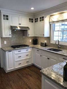 a kitchen with white cabinets and granite counter tops, wood flooring and a window