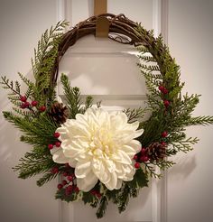 a wreath with white flowers and pine cones hanging on a door