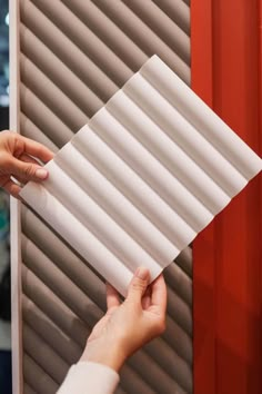 a person holding up a piece of white paper in front of a red wall with shutters