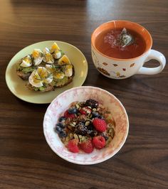 two plates with food on them next to a cup of tea and a bowl of fruit