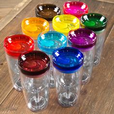 six different colored glasses sitting on top of a wooden table