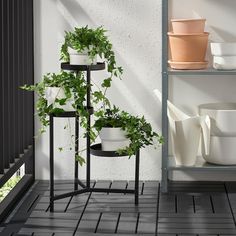 three plant stands with plants on them in front of a white wall and black floor