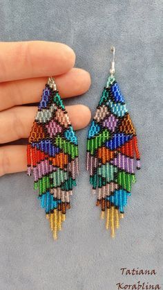 a pair of multicolored beaded earrings in the shape of a triangle on a finger